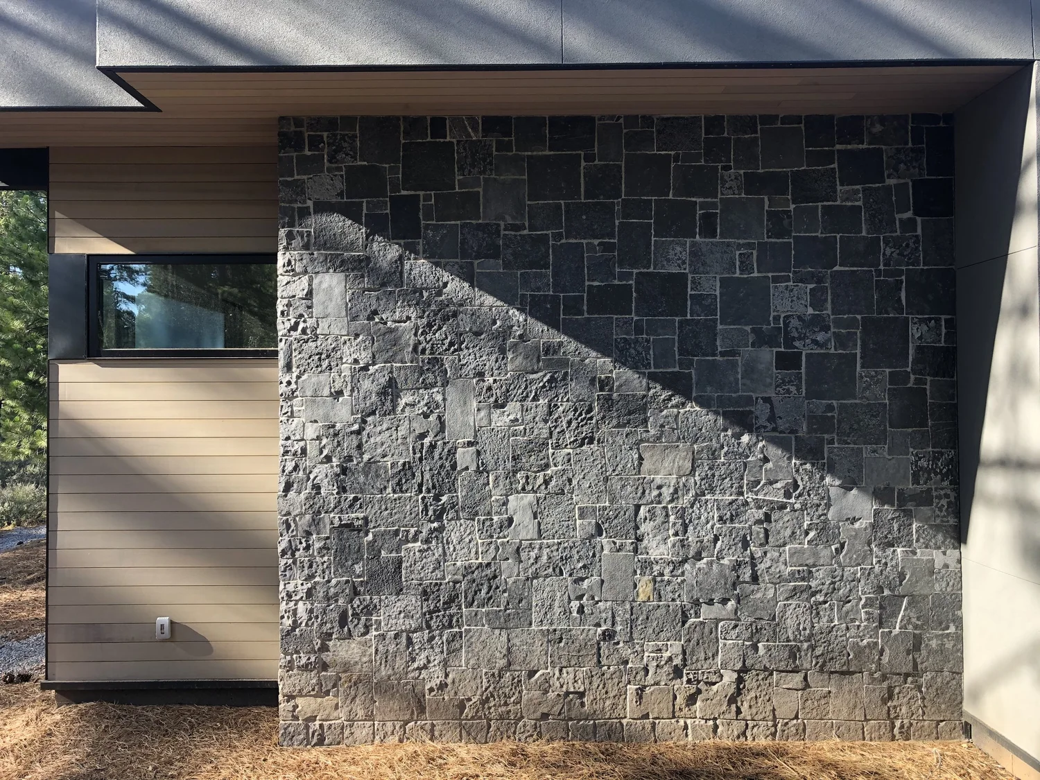 Black Pearl clads a full exterior bay beside horizontal wood siding, a low sun raking a diagonal across the split faces.
