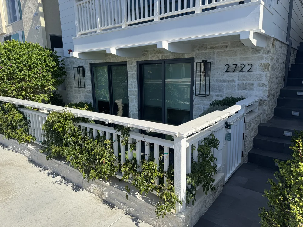 Blue runs the base of a beach house behind a white picket fence, its overgrout softening the coursing.