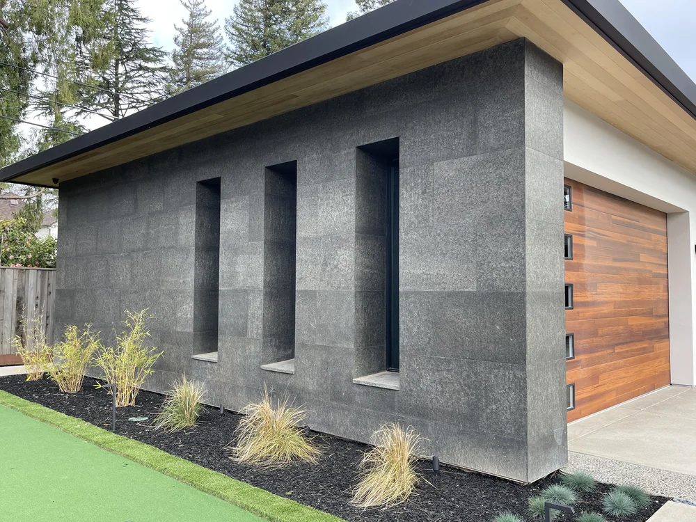 Black Basalt panels wrap a windowless studio volume, three deep reveals cut into the face.