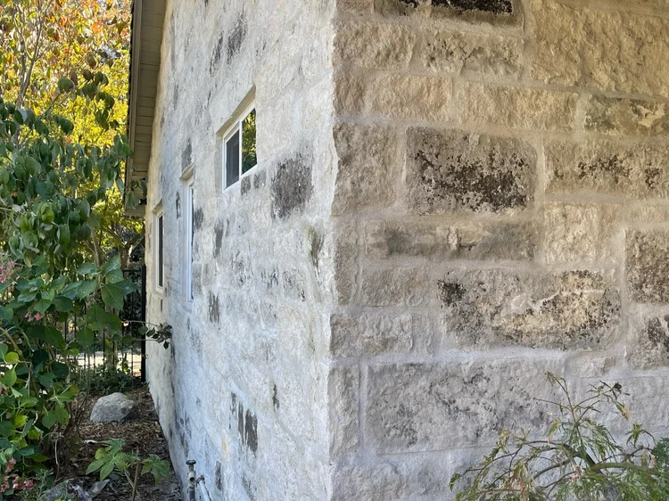 Blue turns the corner of the house in overgrouted courses, small windows punched into the wall.