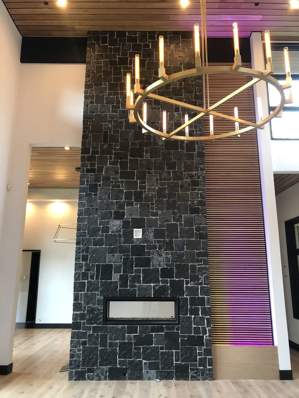 Black Pearl runs a chimney breast the full height of a double volume interior above a linear firebox, a ring chandelier hung against the slatted ceiling.
