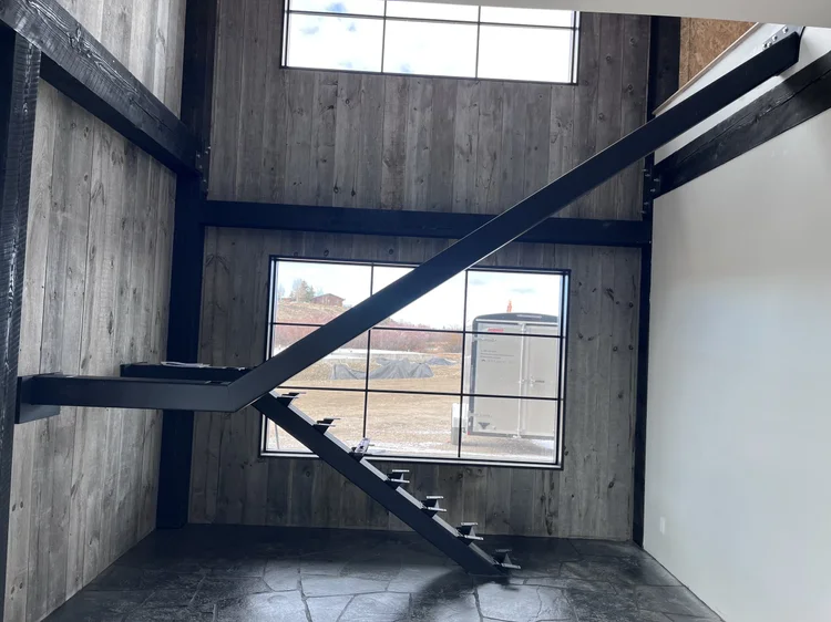 Black Slate paves the floor of a double height room beneath a steel stair stringer and tall windows.