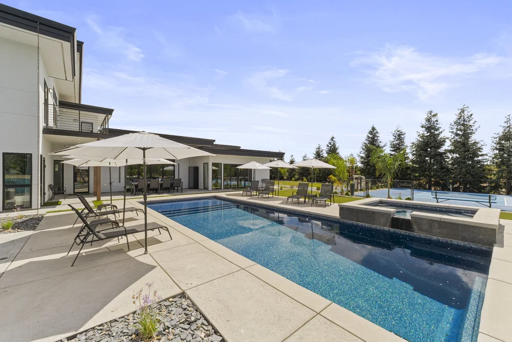 The pool terrace runs the length of the house, Black Basalt beyond the umbrellas.