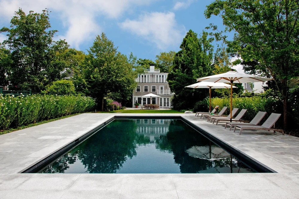 Flamed Woodbury Gray decking runs the full length of a lap pool to a white clapboard house.
