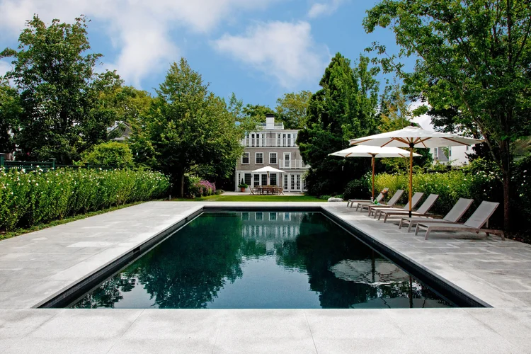 Flamed Woodbury Gray decking runs the full length of a lap pool to a white clapboard house.