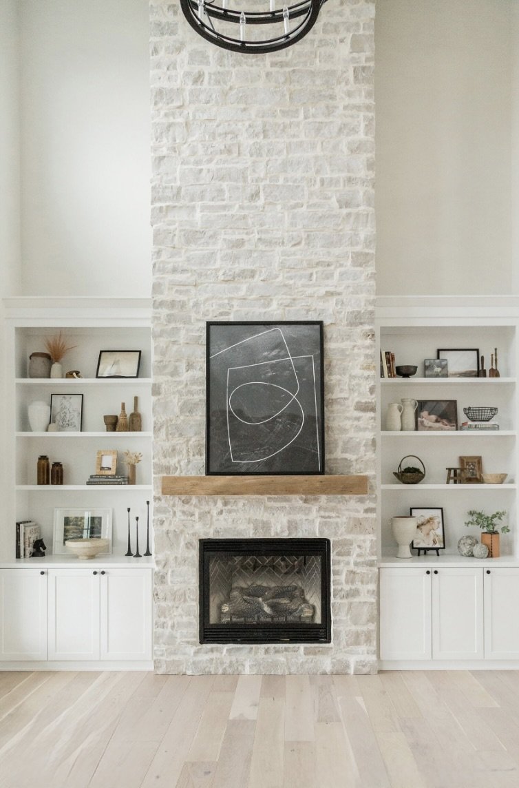 Byron ashlar veneer in a heavy overgrout rises floor to ceiling around a firebox, carrying a timber mantel between white built-ins.