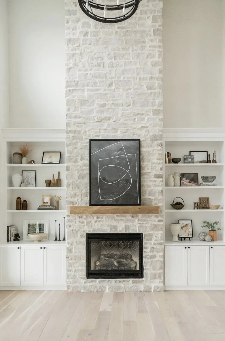 Byron ashlar veneer in a heavy overgrout rises floor to ceiling around a firebox, carrying a timber mantel between white built-ins.