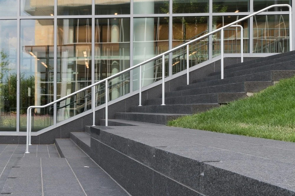 Cambrian Black treads and risers climb between white handrails against a glass facade.
