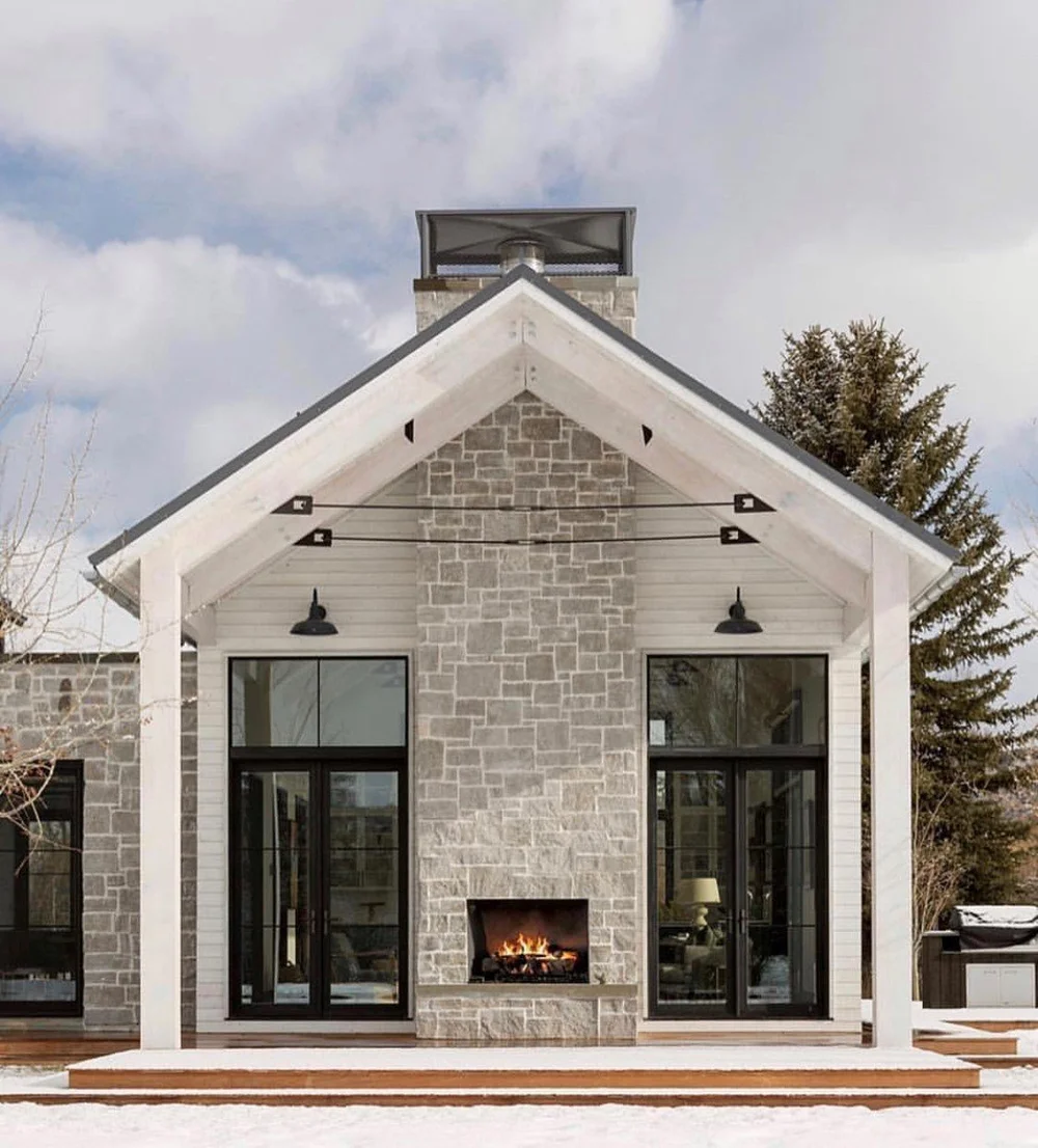 Flint Hills Gray builds the chimney mass of a gabled outdoor room, its firebox lit between black framed doors.