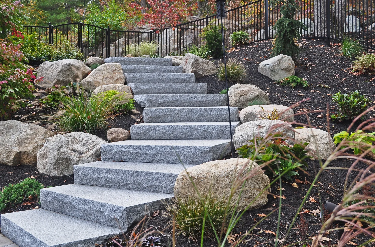 Solid Woodbury Gray steps climb a boulder planted slope to an iron rail.