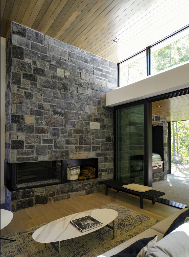 Graphite castle veneer rises to a plank ceiling around a linear firebox and its stacked wood niche.