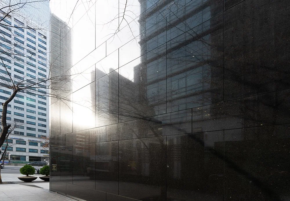 Polished Cambrian Black turns a tower corner, the surrounding city and a low sun caught in its reflection.