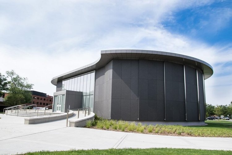 Cambrian Black in flamed panels wraps the curved drum of a museum, meeting the glazed entry at the ramp.