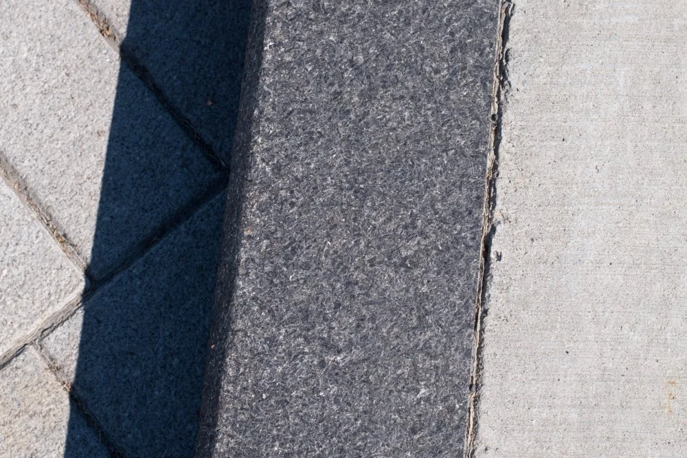 A flamed Cambrian Black curb divides the concrete walk from the roadway, its chamfered arris catching the light.