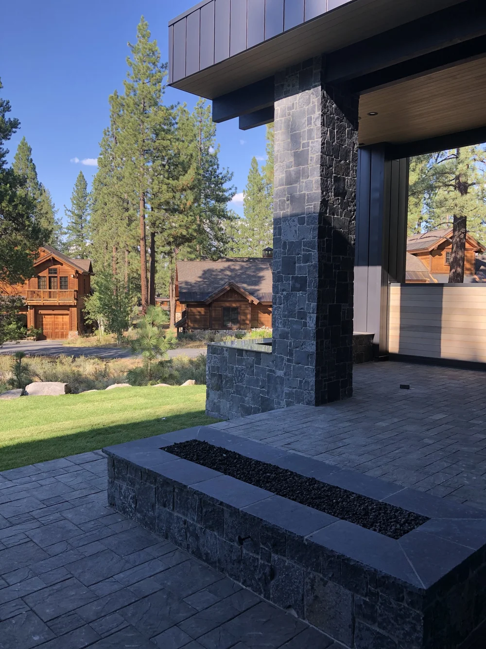 A Black Pearl pier carries the roof above a paved terrace, its stone continuing into the long linear fire feature at the step.