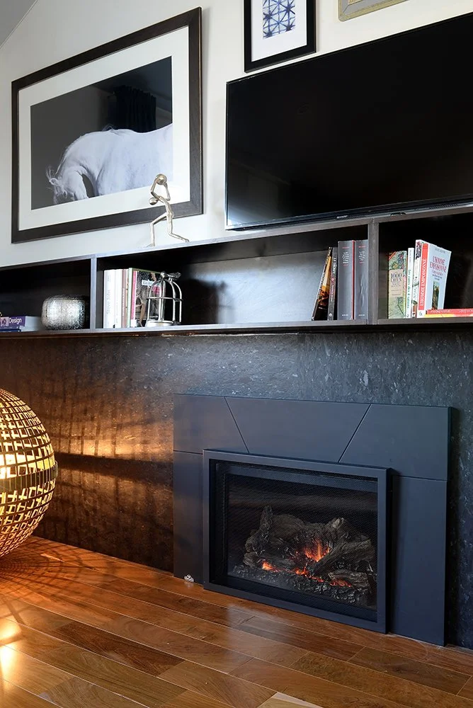Close view of Saint Henry Black panel veneer beside a steel-surround gas firebox, the antique face catching lamplight across its surface.