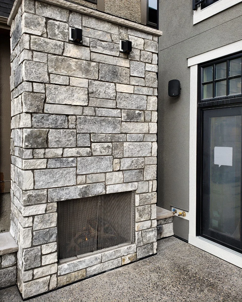 Blue wraps an outdoor firebox in tight gray courses, downlights washing the chimney face above.
