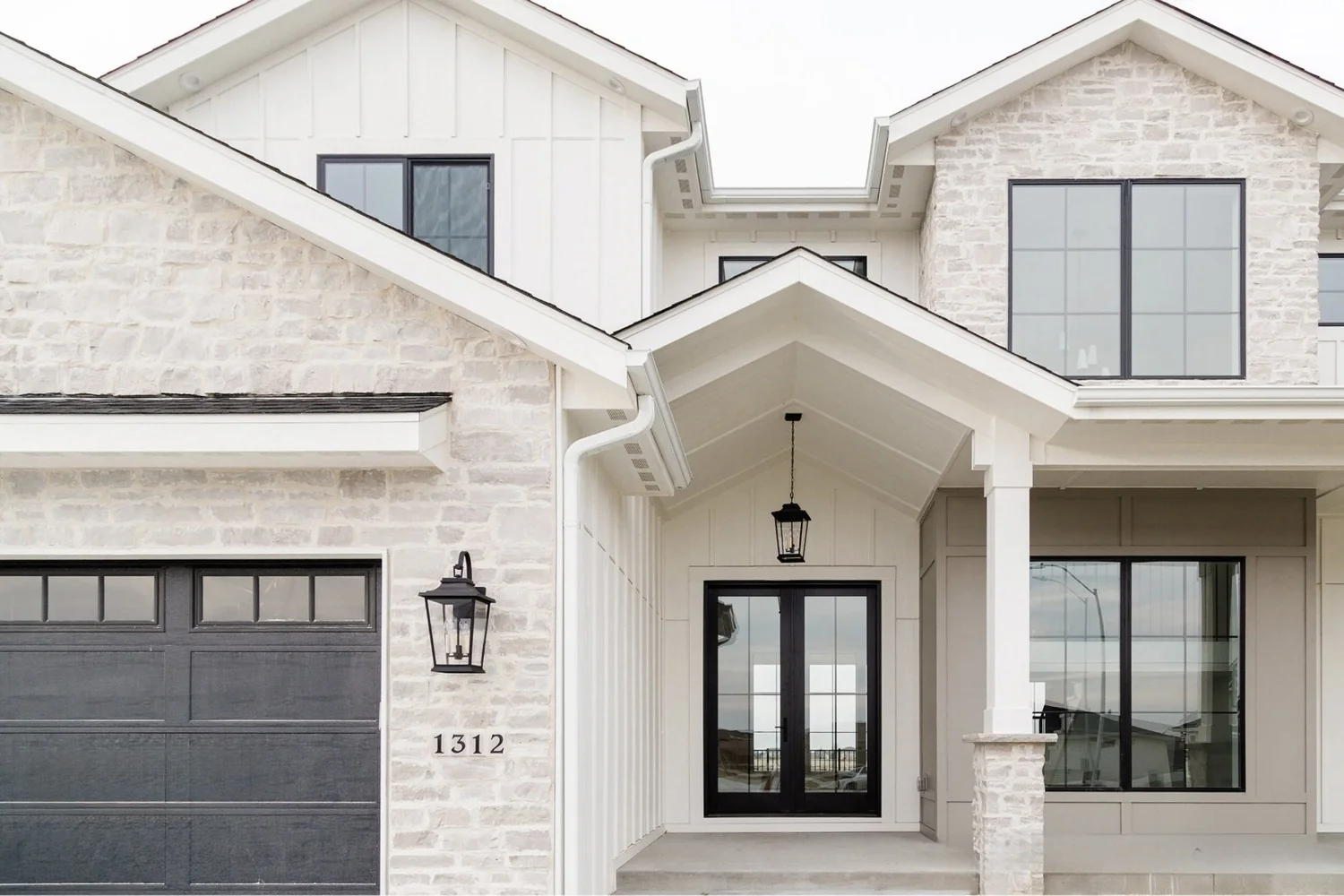 Byron ashlar veneer in an overgrout joint meets white board and batten across a farmhouse entry with a dark garage bay and black lanterns.