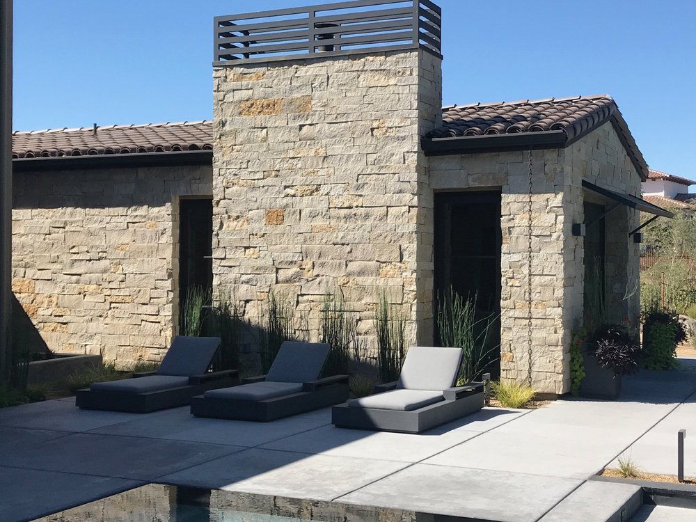 Buff coursed veneer in split and natural faces with dry-stack joints on a pool facade with an outdoor fireplace.