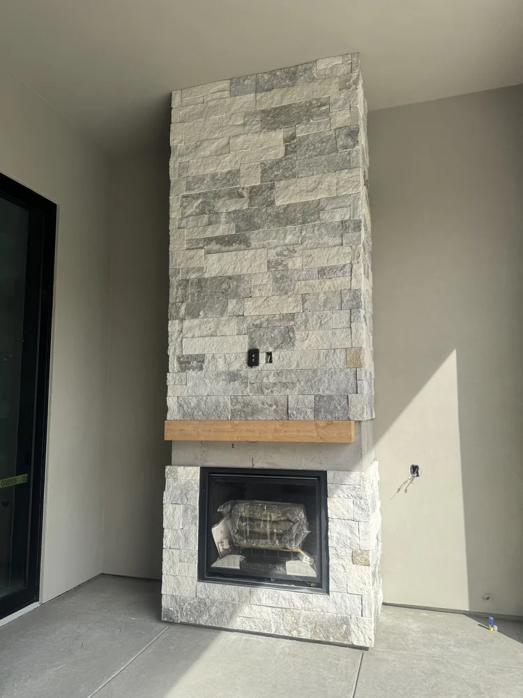 Blue climbs a chimney breast to the ceiling above a timber mantel and black firebox, dry stacked in cream and gray.