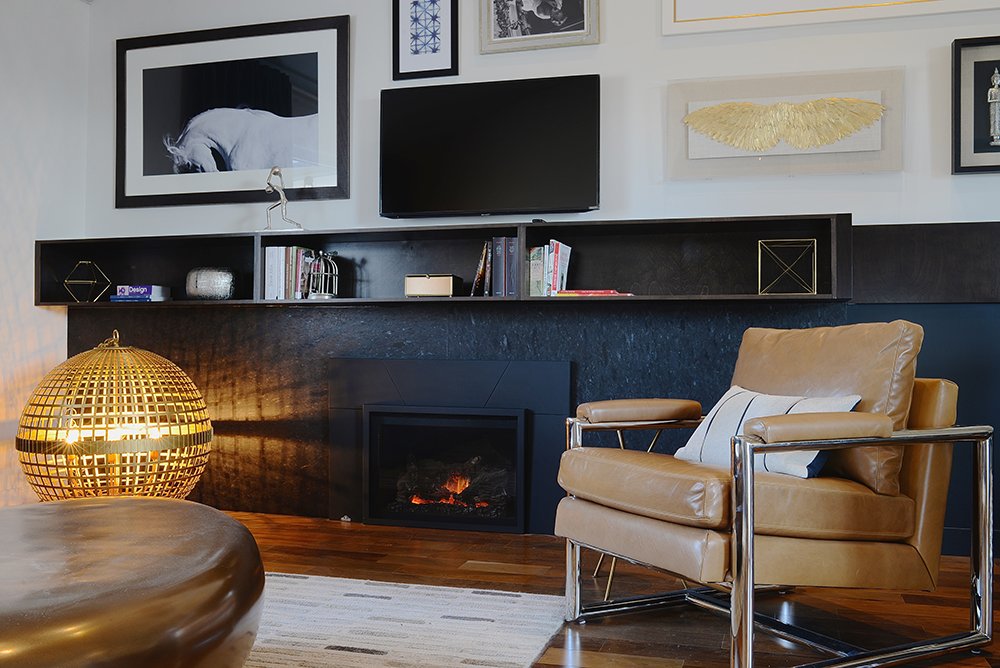 Saint Henry Black panel veneer running the full width of a low fireplace wall in a midcentury living room, a floating shelf above and a tan leather chair alongside.