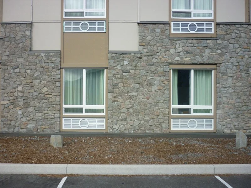 Grizzly mosaic wraps the ground floor of a hotel elevation beneath tan panels and grid windows.