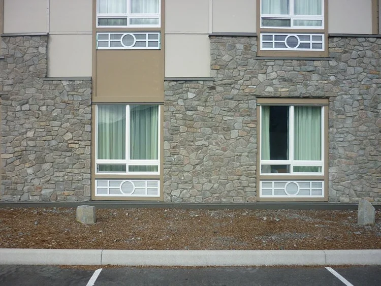 Grizzly mosaic wraps the ground floor of a hotel elevation beneath tan panels and grid windows.