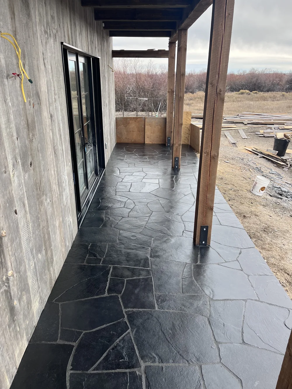 Black Slate flags a covered walk in irregular paving, running the length of a board sided wall between timber posts.