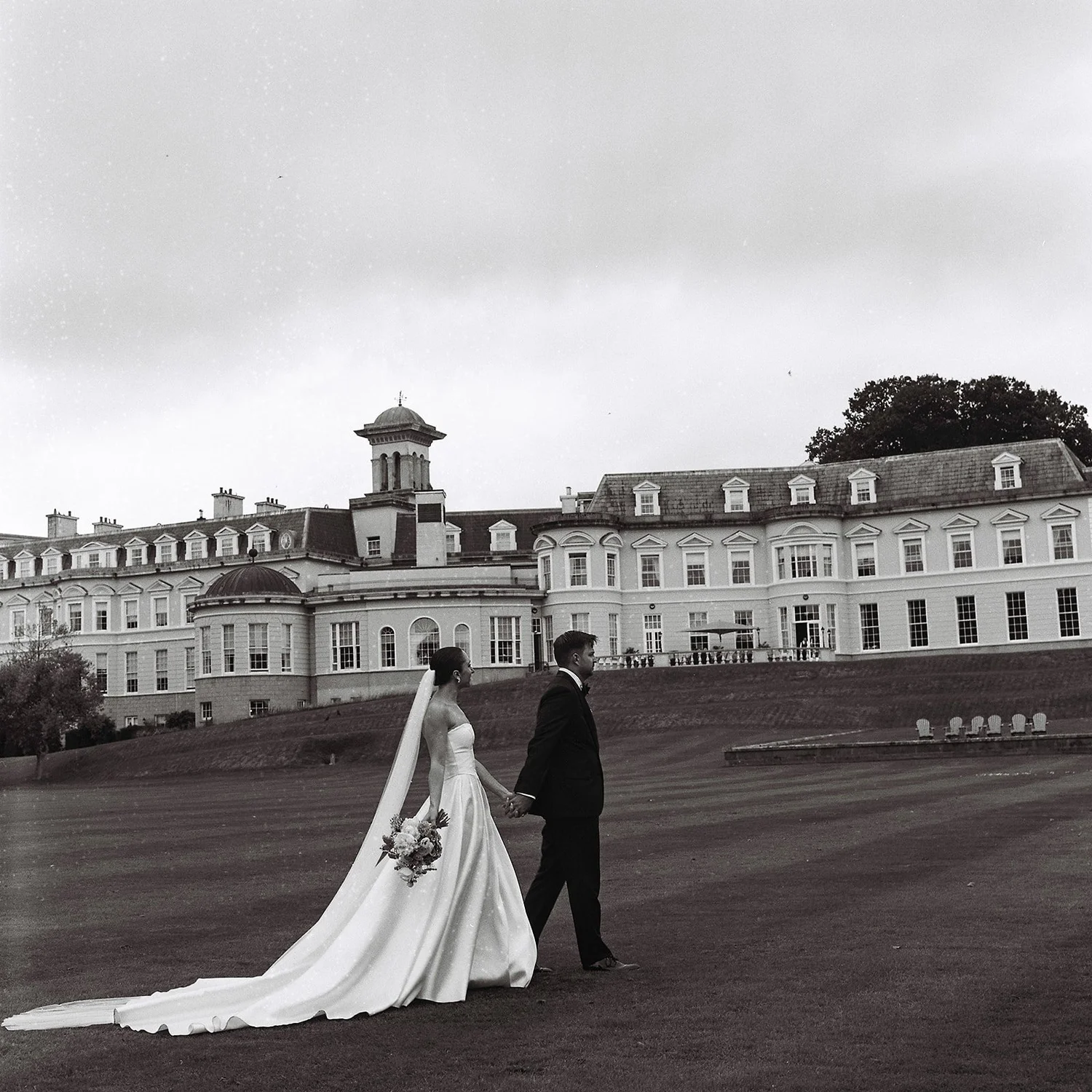 Black and white film photograph of a couple walking across the lawn in front of The K Club