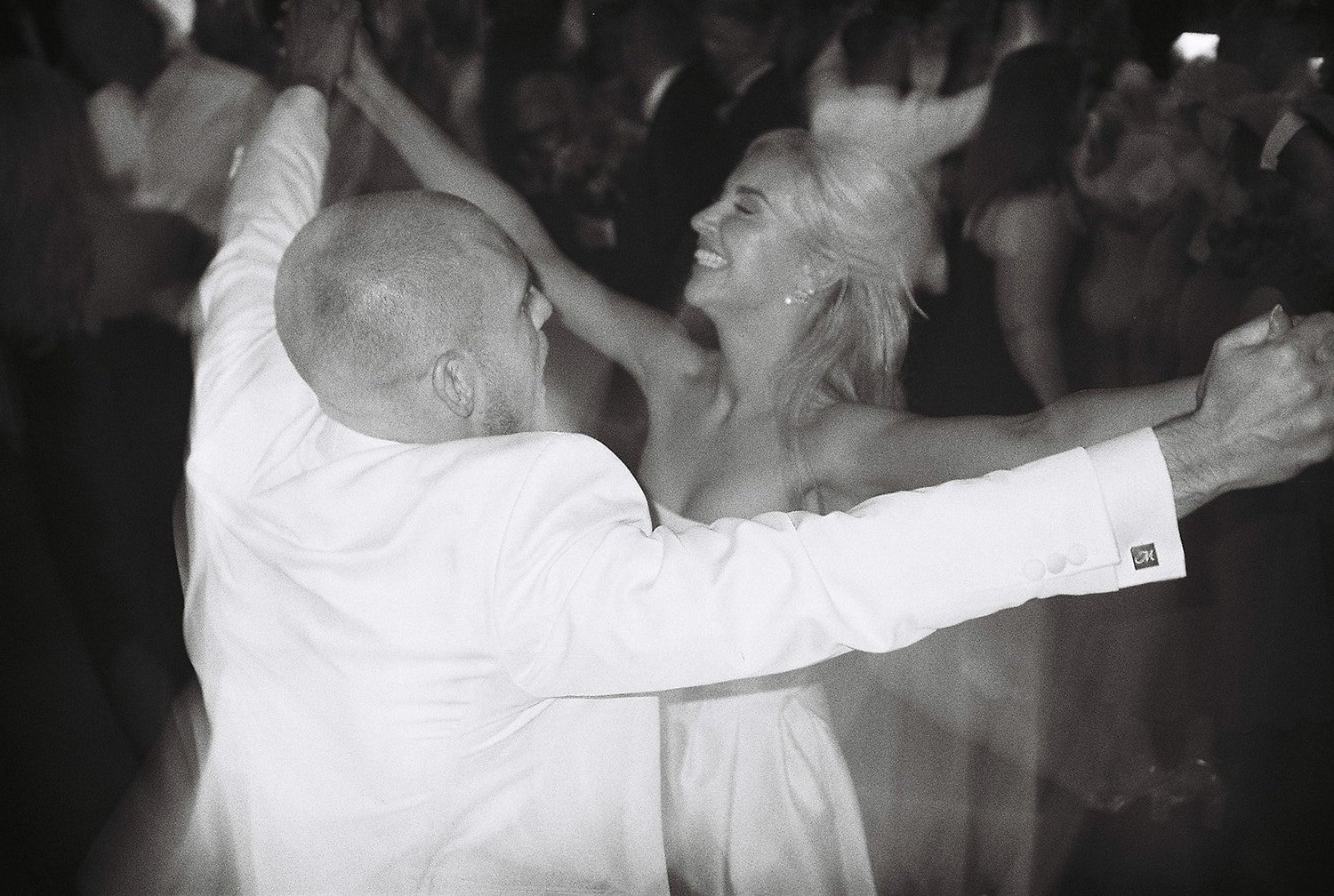Black and white film photograph of guests dancing with their arms in the air at a Dublin wedding