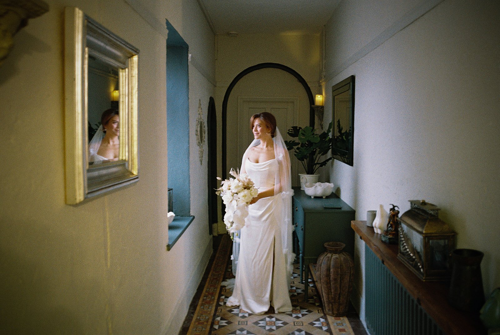Bride standing in a sunlit hallway beside a gilt mirror, photographed on film