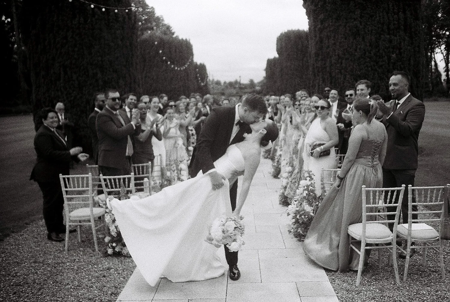 Black and white film photograph of a couple kissing in the aisle as guests cheer at a Kildare wedding