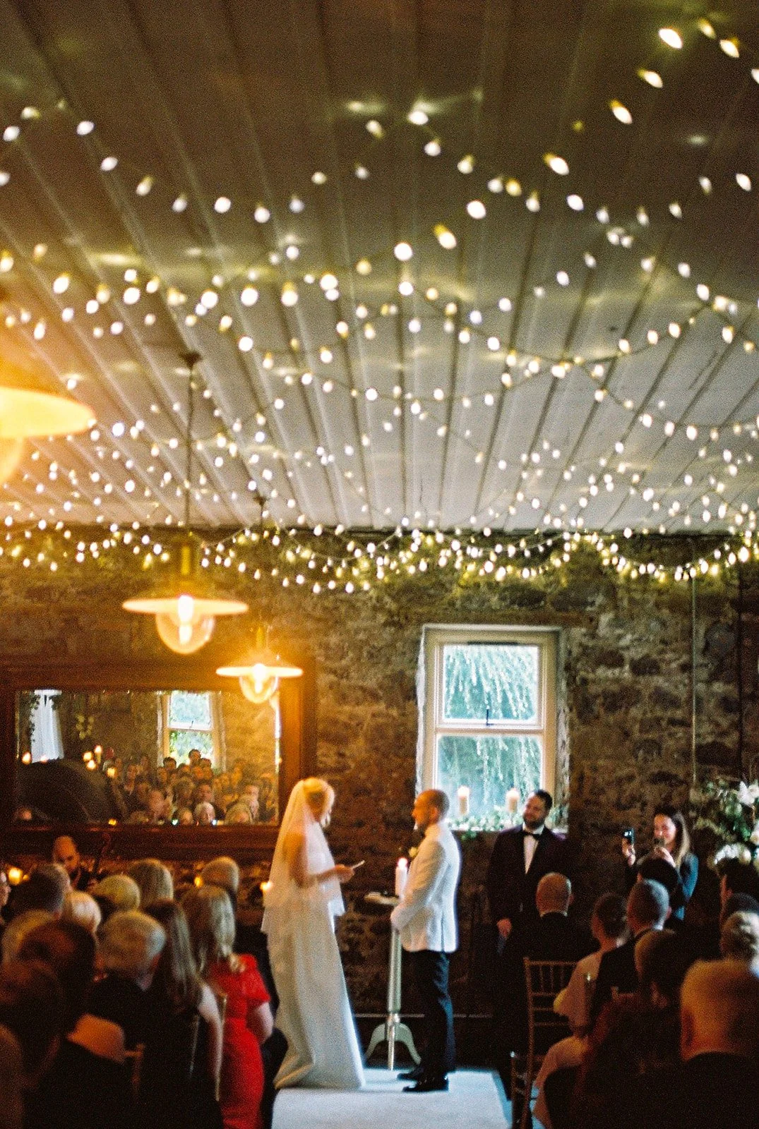 Ceremony under strings of fairy lights in a stone-walled room, photographed on film