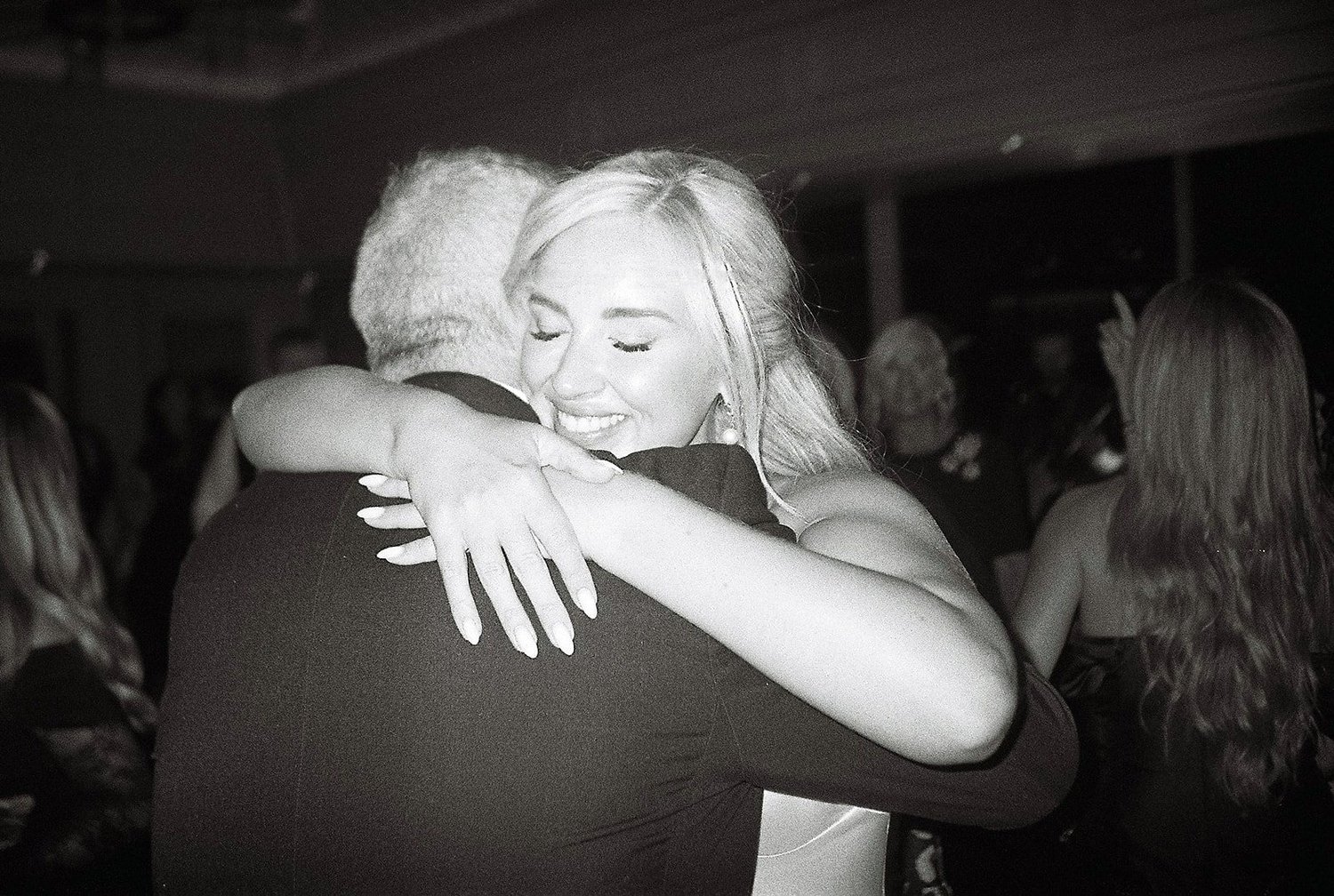 Black and white film photograph of a bride hugging a guest on the dance floor