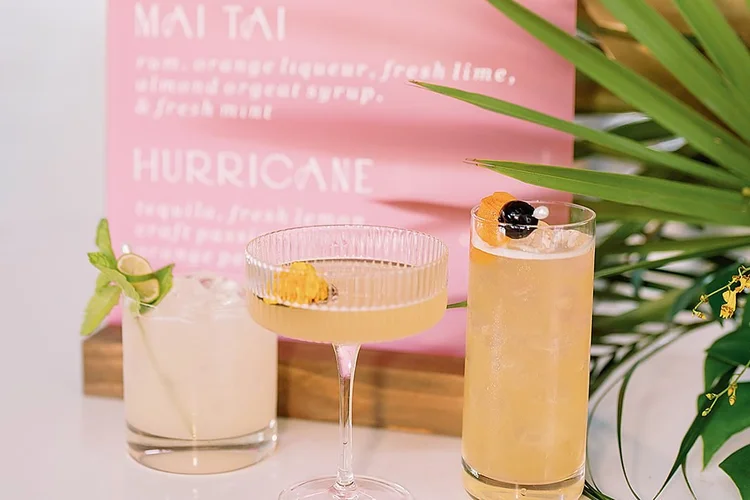 A pink custom drink menu on the bar with three finished cocktails in front of it