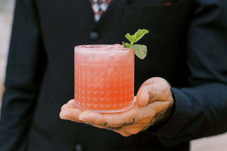 A Drink Slingers bartender holding out a pink signature cocktail with a mint garnish