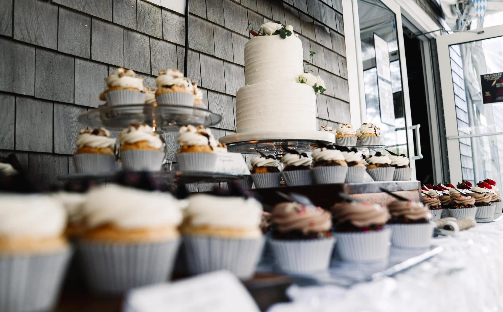 A wedding cake surrounded by cupcakes at Naukabout