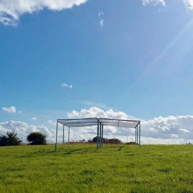  A single rain shelter in a grassland field. Sun rays are hitting it. 