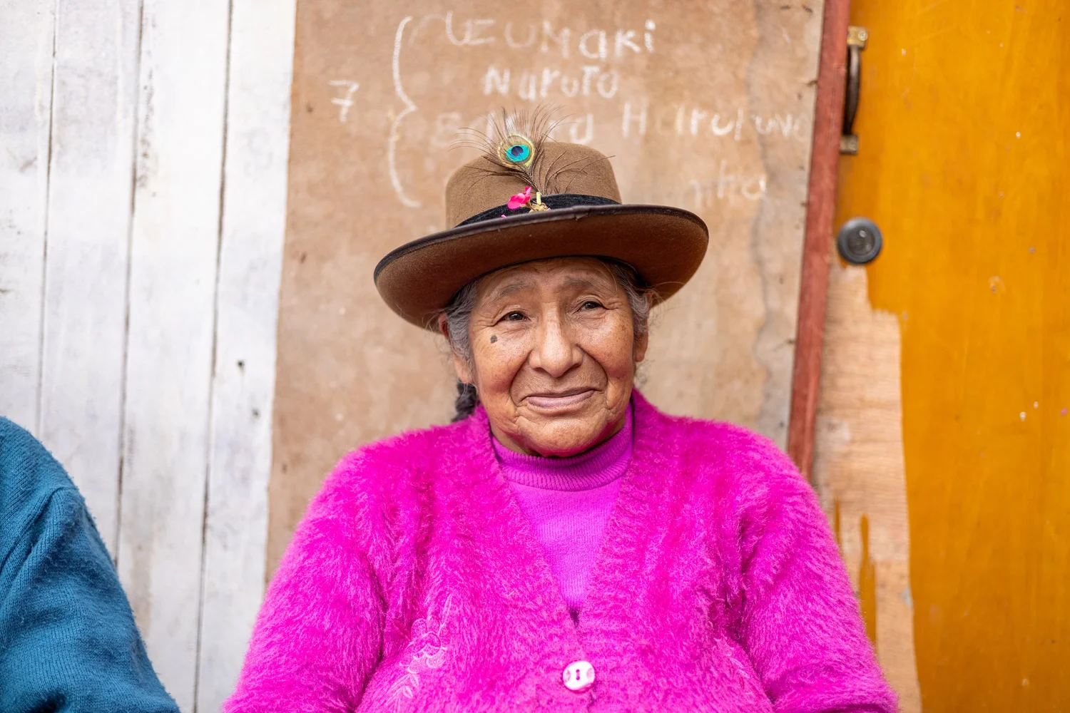 An older woman wearing a brown hat and bright pink cardigan at a doorway