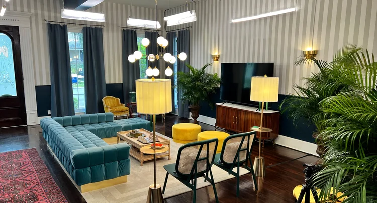 Eclectic styled living room with a teal velvet sectional, globe chandelier and linear LED pendants in the Real World New Orleans house