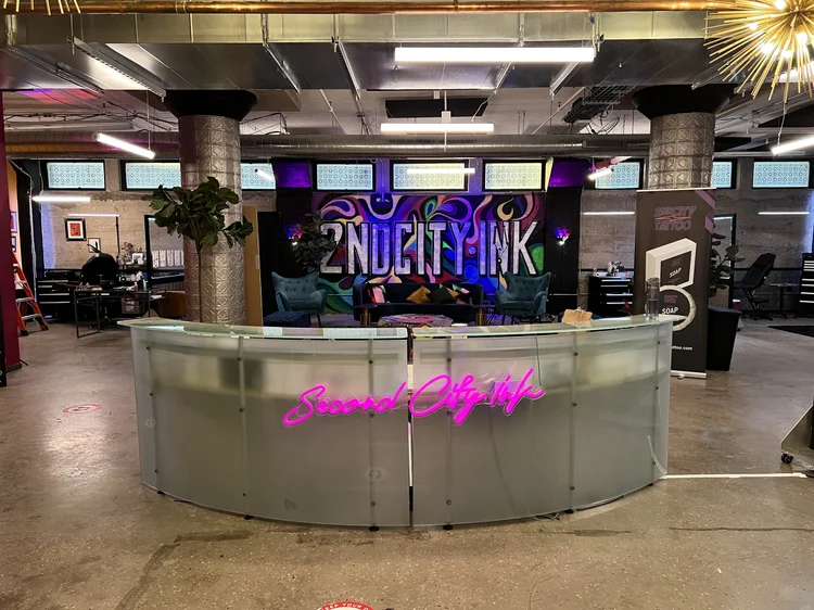 Reception desk and neon sign at the 2nd City Ink (Black Ink Chicago) shop build, lit by The Camera EYE