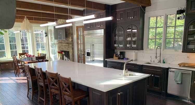 Open-plan kitchen and breakfast room with a stone fireplace and suspended linear LED pendants in the Black Ink Atlanta house