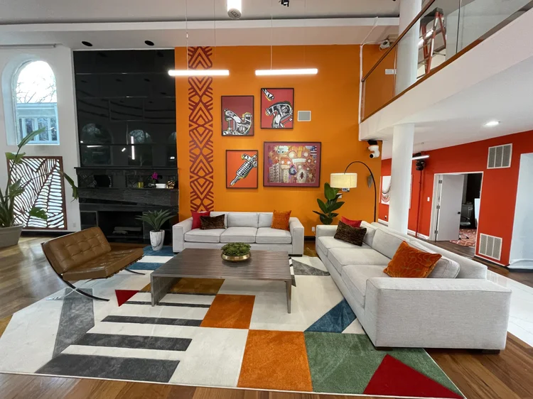 Double-height living room with an orange feature wall and suspended linear LED lighting in the Black Ink Atlanta house, designed by The Camera EYE