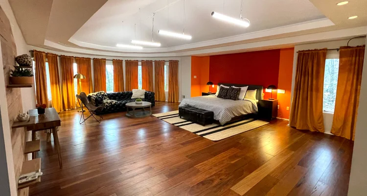 Spacious primary bedroom with a rust feature wall and suspended linear LED lighting in the Black Ink New York (East Hills) house