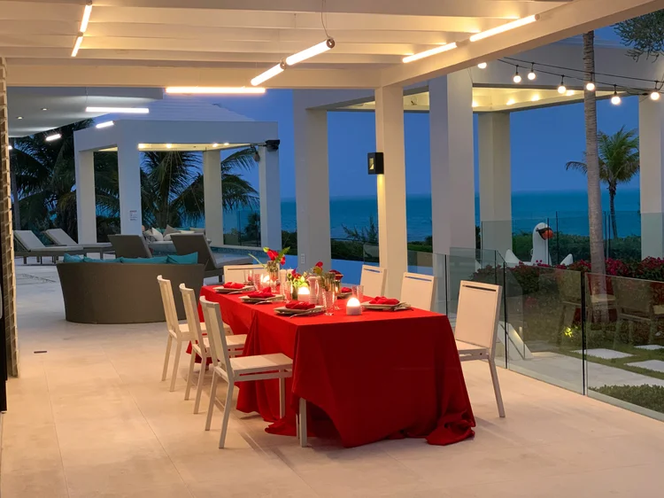 Oceanfront covered terrace at dusk set for dinner, with automated beam and festoon lighting at the Turks & Caicos villa