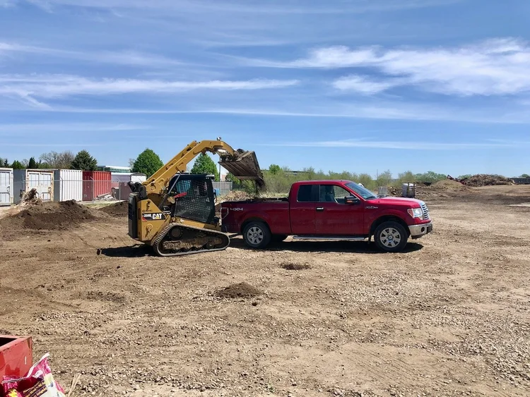 Skid steer loading compost into the bed of a red pickup at the Soil Dynamics yard