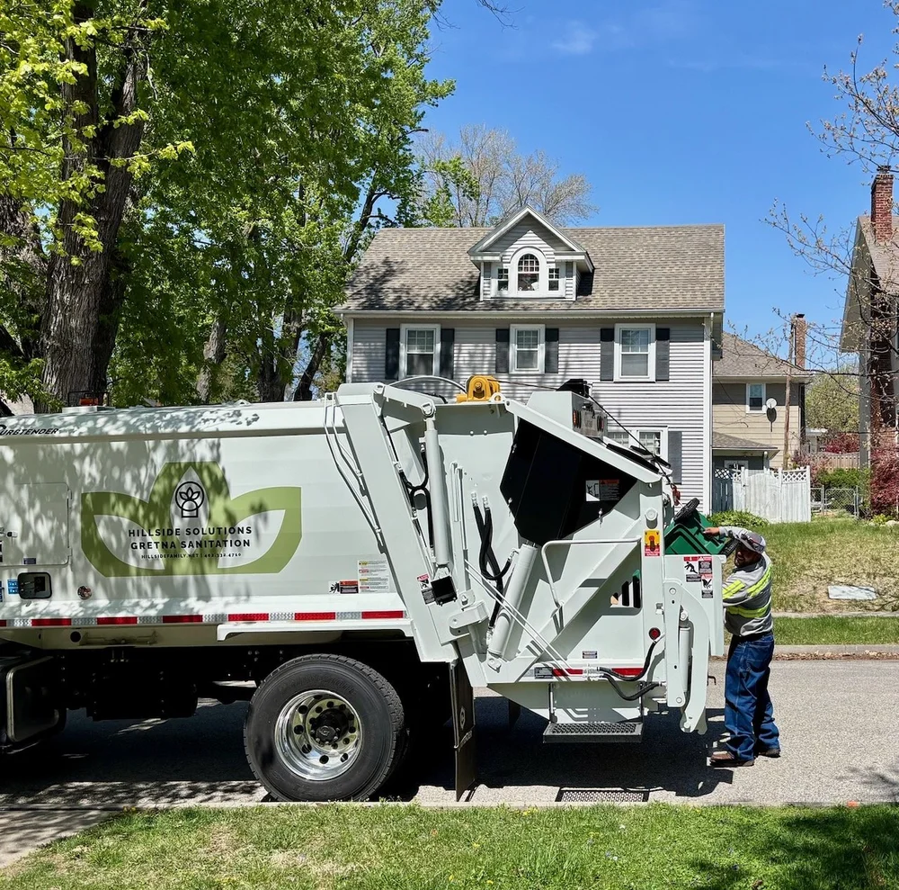 A Hillside Solutions and Gretna Sanitation truck collecting a green cart at the curb in Omaha