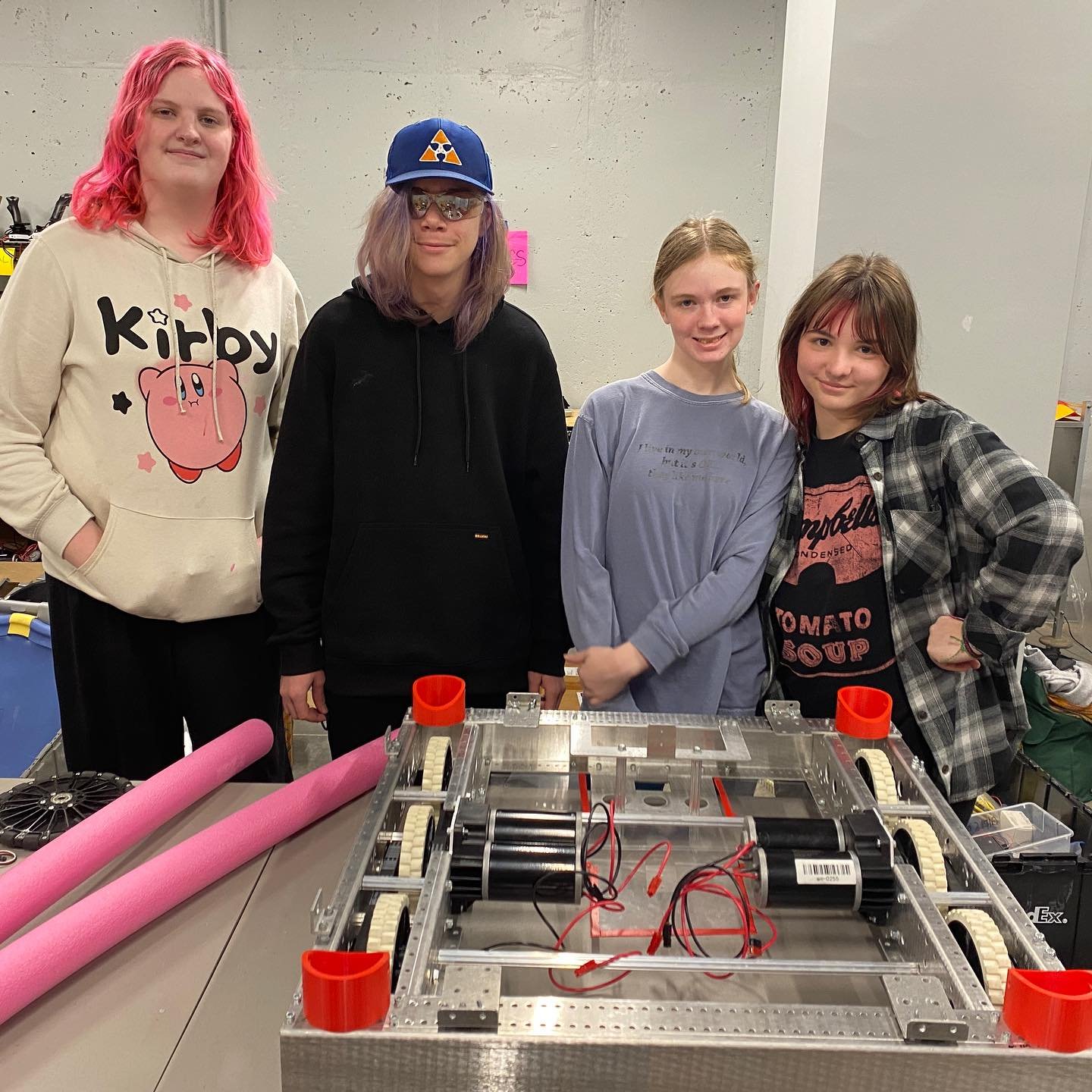 Three Girls on Fire students and one Triple Strange student working on a robot base that is about 3 feet by 3 feet in size
