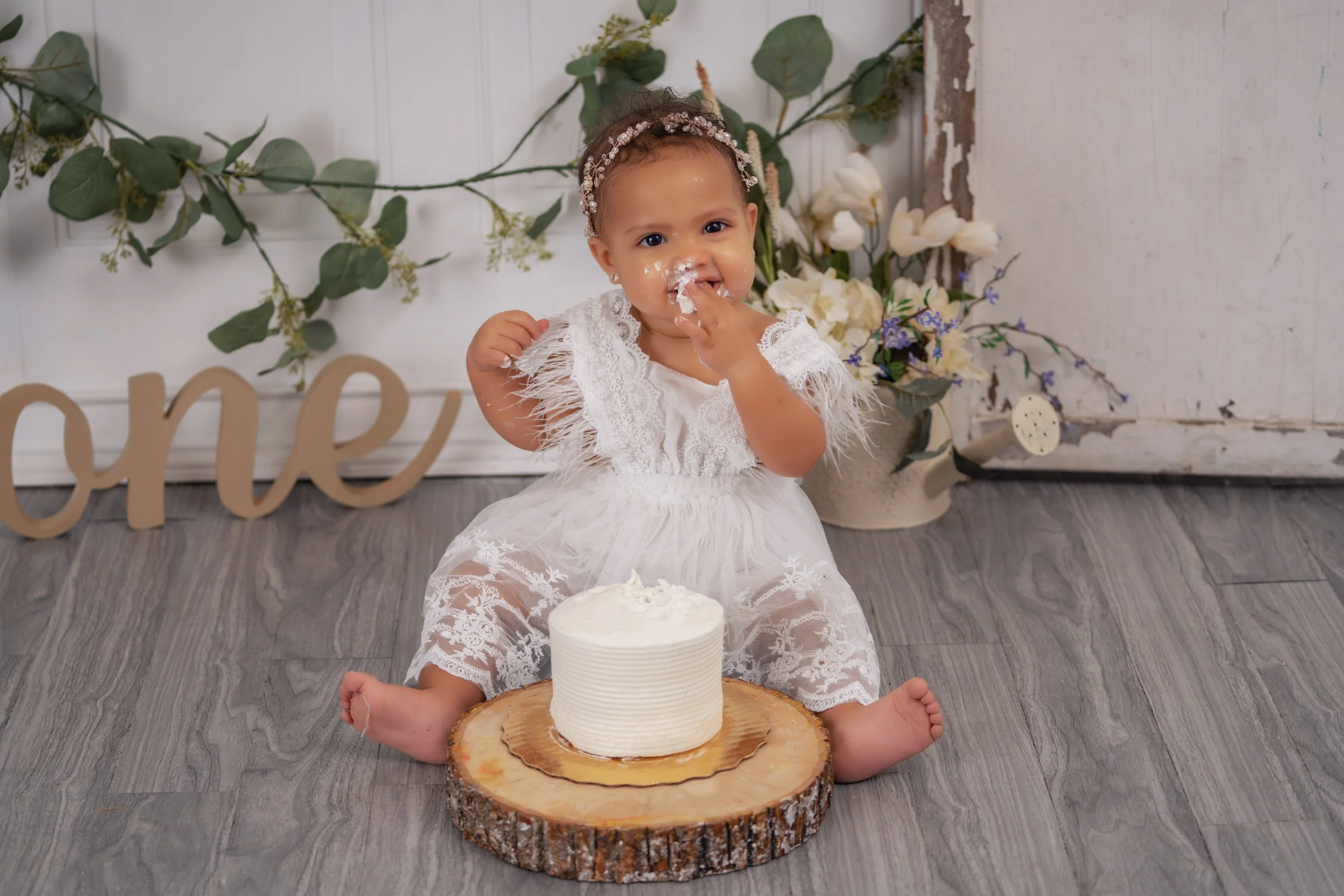 Baby tasting frosting beside a white first birthday cake in the Chattanooga studio