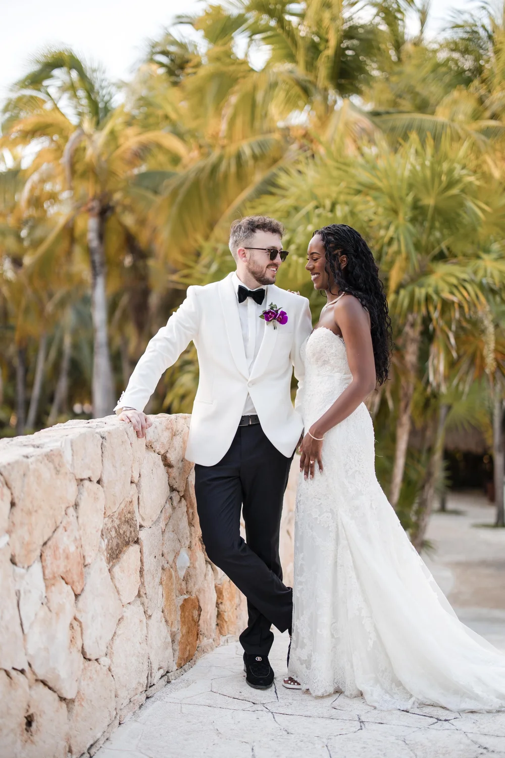 A couple on a stone terrace lined with palms, the groom in a white dinner jacket